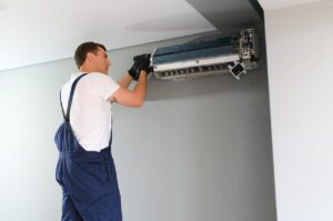 A man in overalls repairs an air conditioner, demonstrating his skills in home maintenance and appliance repair.