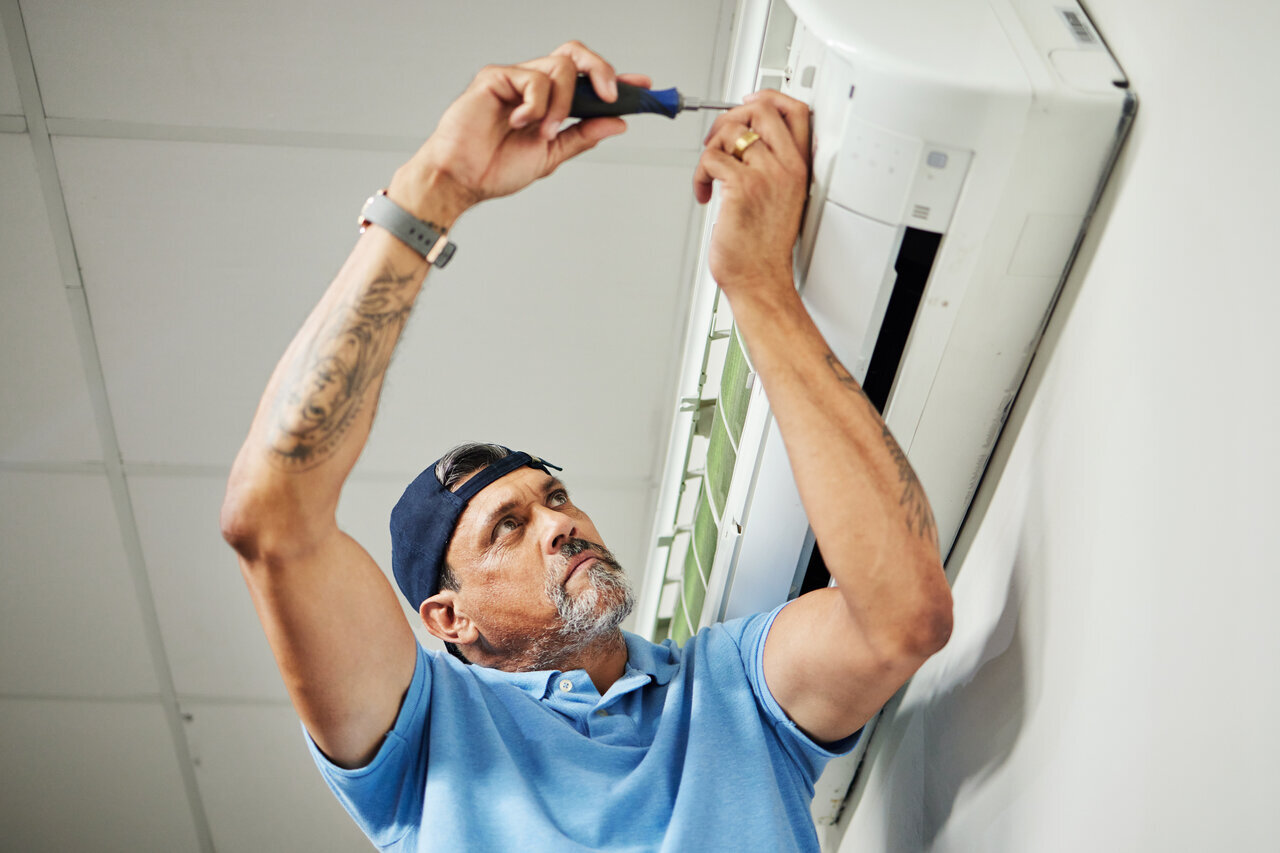 A technician repairing an air conditioning unit, focused on ensuring optimal performance and efficiency.